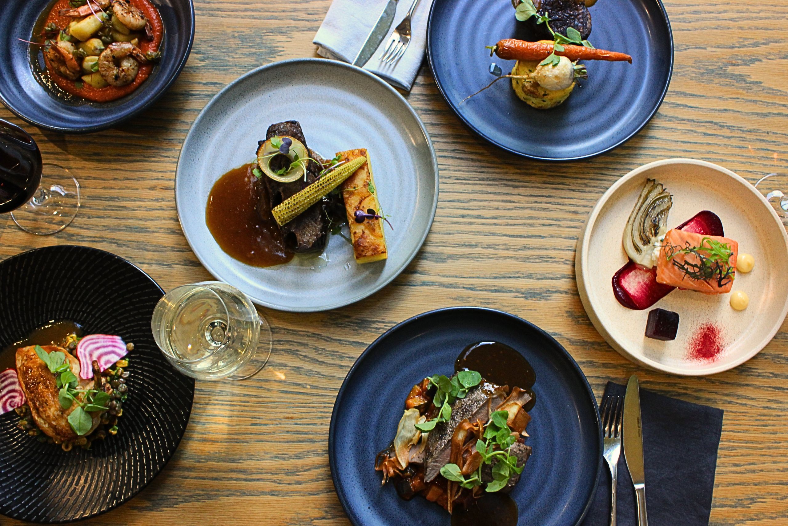a selection of entres & mains, including salmon, beef, lamb & gnocchi. set on a table with cutlery, glassware & wine