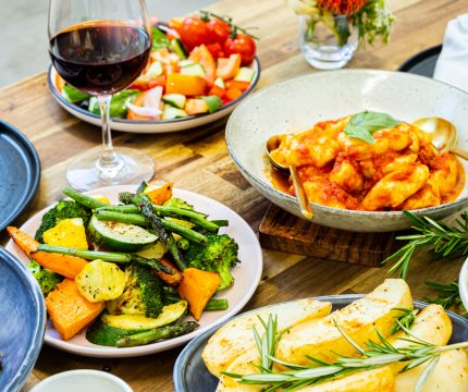Authentic Italian buffet catering. Laid out on a wooden table are seasoned vegetables, pasta dishes, salads and red wine.