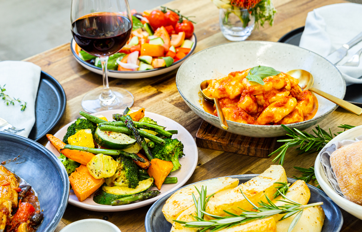 Authentic Italian buffet catering. Laid out on a wooden table are seasoned vegetables, pasta dishes, salads and red wine.